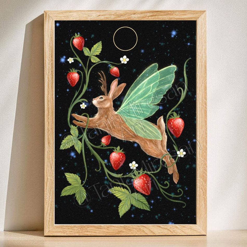 A framed art print featuring a whimsical illustration of a brown fairy rabbit with green wings flying among strawberry vines on a black starry background, set in a light wood frame and leaning against a wall.