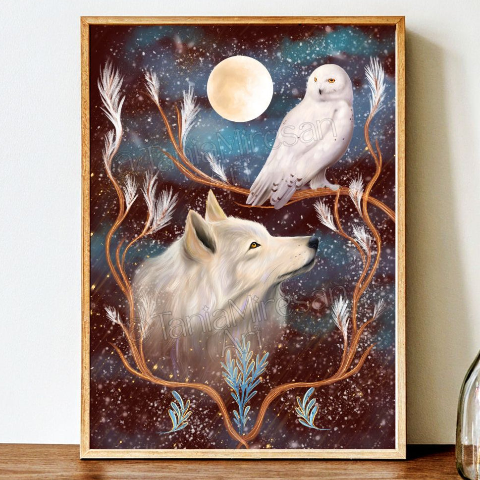 A framed art print featuring a white wolf and a snowy owl under a full moon, set against a starry cosmic background with decorative branches, displayed on a wooden surface against a white wall.